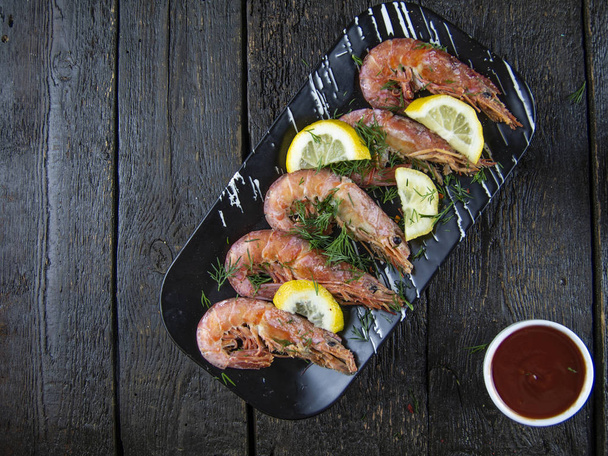 Boiled shrimps with lemons, greens and sauce on a wooden background. - Fotó, kép