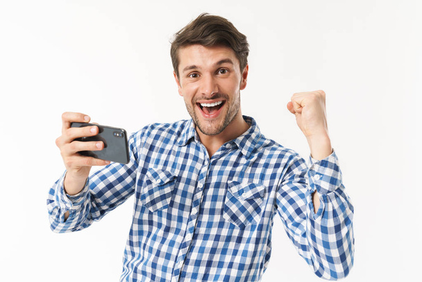 Photo of delighted man in casual shirt playing video game on cellphone and clenching fist - Fotografie, Obrázek