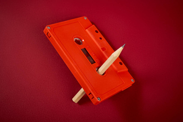 orange audio cassette and pencil on dark red background - Photo, Image