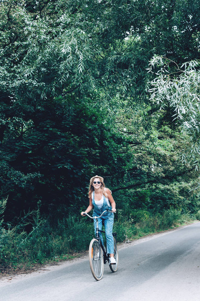 Beautiful teenage girl riding bicycle through the forest or park. - Photo, Image