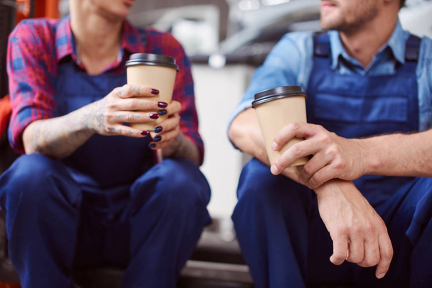 Close up of two automechanics drinking coffee from paper cups. - Foto, Imagen