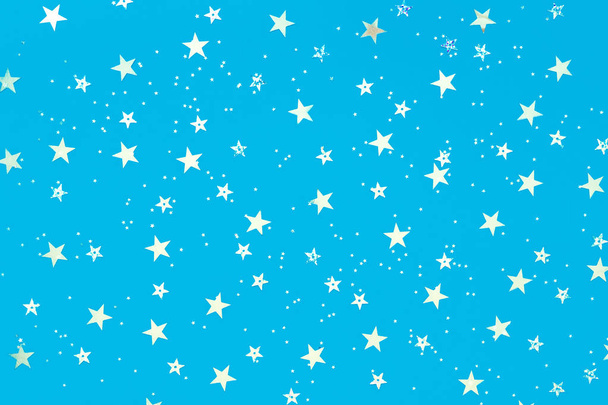 Srebrne gwiazdki posypane na pastelowych niebieskim tle. Świąteczne tło wakacyjne. dla Twoich projektów. Koncepcja obchodów. Wzór świąteczny. Widok z góry, płaski lay - Zdjęcie, obraz