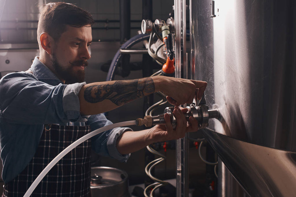 Brewery worker puts on a pipe onto the tap. - Foto, immagini