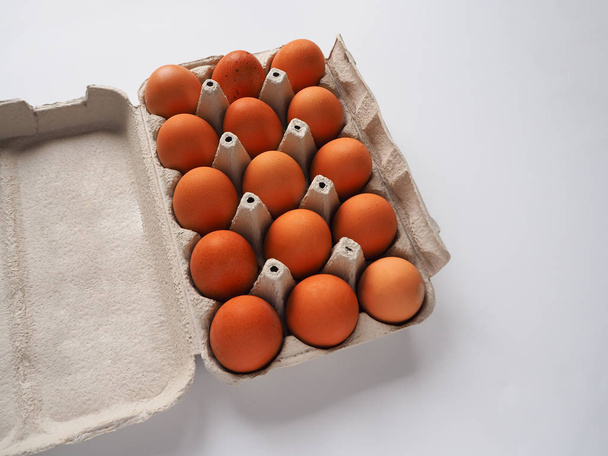 Csomag 15 barna friss nyers csirke tojást egy fehér karton tojás dobozban egy fehér háttér közelről. - Fotó, kép