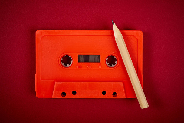 Oranje audio cassette en potlood op donker rode achtergrond - Foto, afbeelding