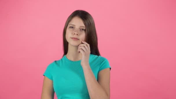Młoda dziewczyna myśli w studiu na różowym tle. Zwolnionym - Materiał filmowy, wideo