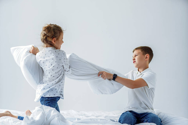 Naughty twins girl and boy friendly fighting staged a pillow fight on the bed in the bedroom. - Zdjęcie, obraz