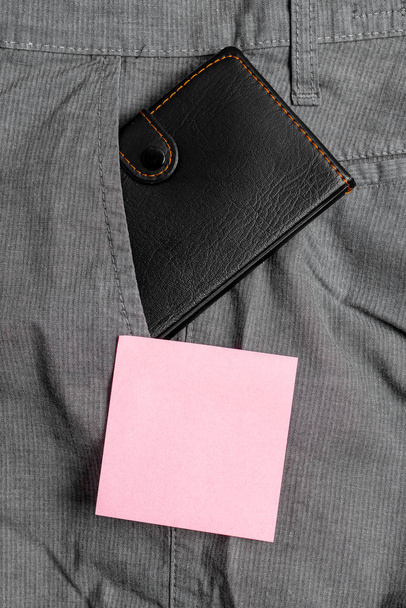 Pembe not kağıdı yanında pantolon ön cebinde küçük cüzdan. Küçük çanta notasyon levha yakın erkek pantolon içine yerleştirilir. Düz döşeme fotoğrafçılığı düzenleme sanatsal yolu - Fotoğraf, Görsel
