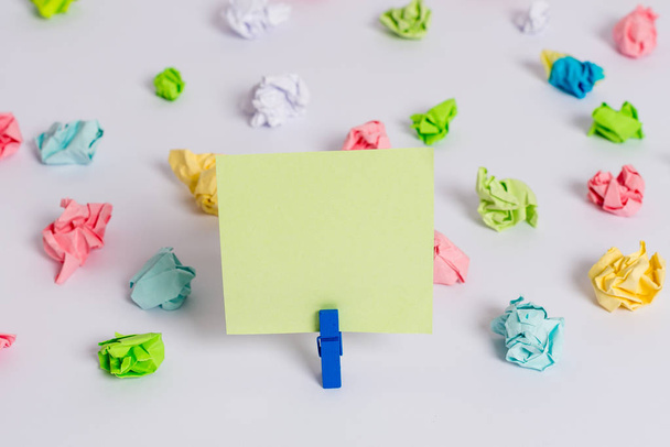 Colored crumpled sheets placed around the empty rectangle square shaped reminder note in the centre of a white floor. Office supplies, blank paper pinned by a fastener. - Photo, image