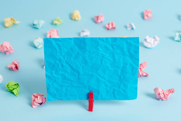 Colorful crumpled papers and rectangle square shaped colored note in a blue background. Red clip hanging a reminder paper in a blank space. Light office table. - Photo, Image