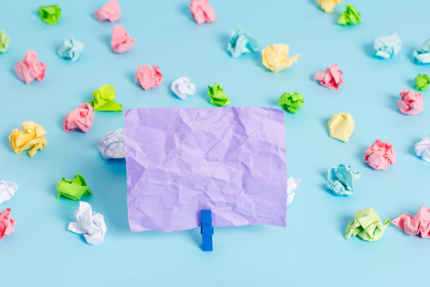 Colored crumpled sheets placed around the empty rectangle square shaped reminder note in the blue background. Office supplies, blank paper pinned by a fastener. - Фото, зображення
