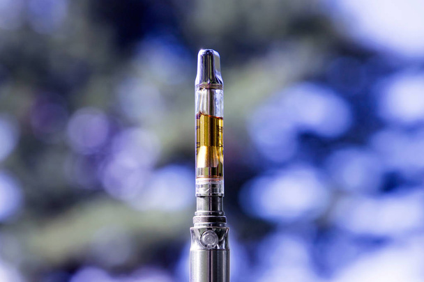 Elektronická cigareta s konopným olejem na rozmazaném přírodním pozadí - Fotografie, Obrázek