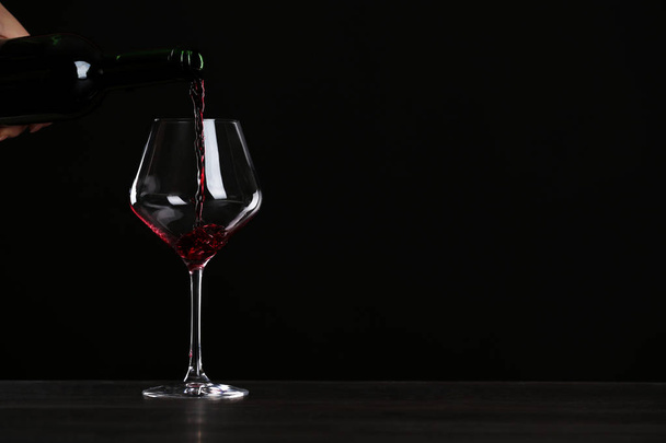 Woman pouring wine into glass on table against black background, closeup with space for text - Foto, afbeelding