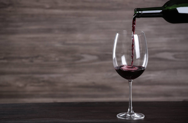 Pouring wine from bottle into glass on table against wooden background, space for text - Fotó, kép