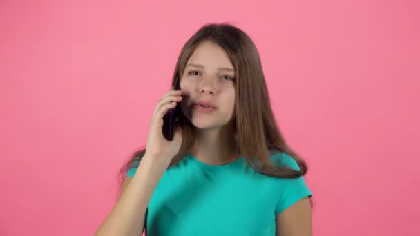 Teen female talking using cell phone in studio against pink background. Slow motion - Πλάνα, βίντεο