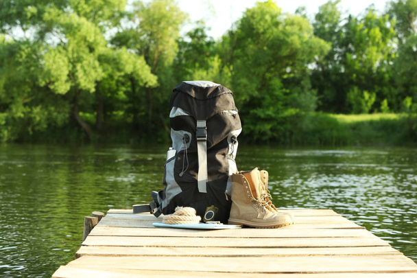 Backpack and camping equipment on wooden pier near river - Φωτογραφία, εικόνα