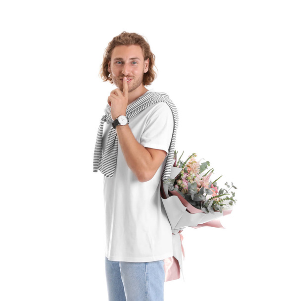Young handsome man hiding beautiful flower bouquet behind his back on white background - Valokuva, kuva