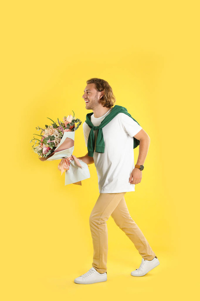 Young handsome man with beautiful flower bouquet on yellow background - Foto, Bild