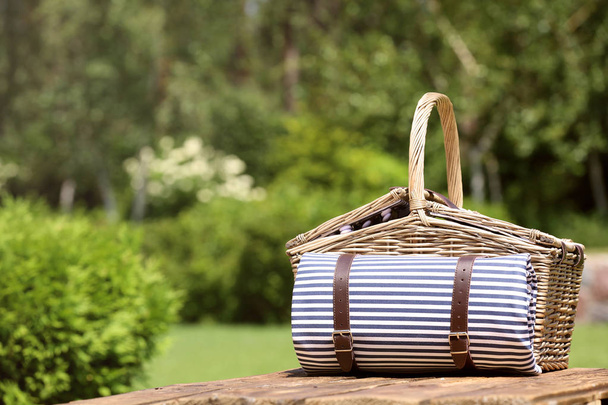 Picnic basket with blanket on wooden table in garden. Space for text - Фото, изображение