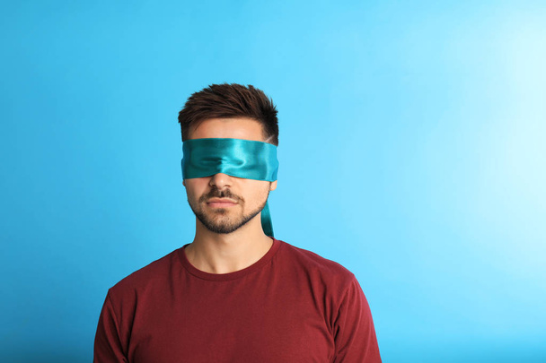 Young man with blindfold on blue background, space for text - Fotó, kép