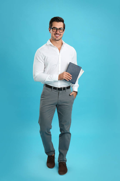 Young male teacher with glasses and notebooks on light blue background - Valokuva, kuva