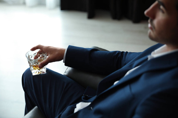 Young man with glass of whiskey indoors, closeup - Fotó, kép