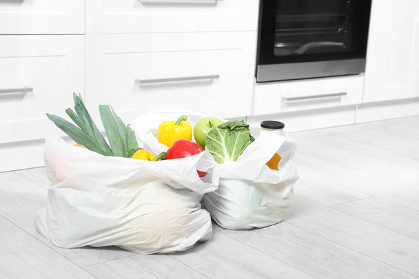 Пластиковые пакеты с овощами и соком на полу на кухне. Пространство для текста
 - Фото, изображение