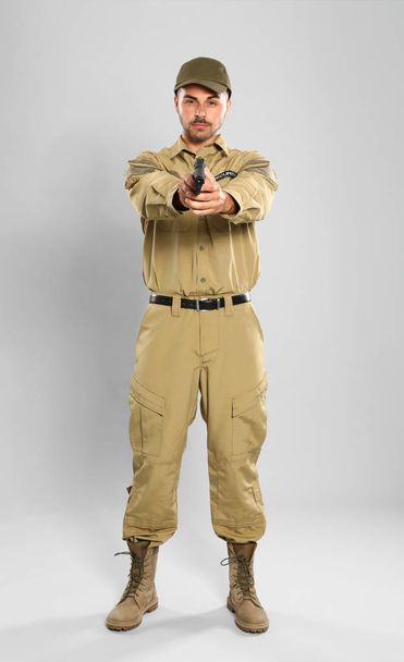 Male security guard in uniform with gun on grey background - 写真・画像