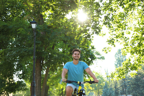 Handsome young man riding bicycle on city street, low angle view - Photo, image