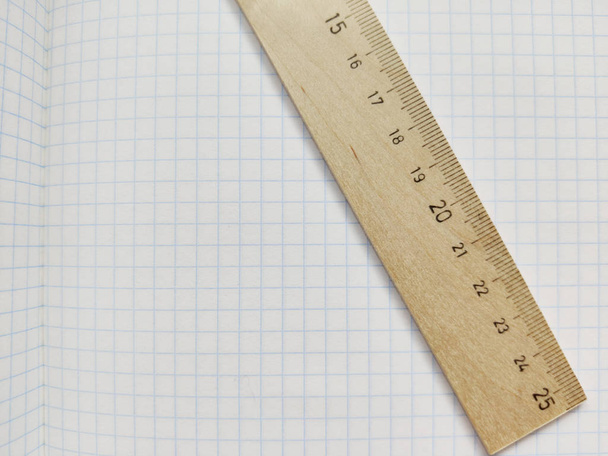 Dřevěný vládce s metrickou soustavou se opírá o bílou šešovanou knihu bez poznámek. Školní zápisník v kleci. Prázdný Poznámkový blok se čtvercovou texturou. Měřicí pravítko - Fotografie, Obrázek