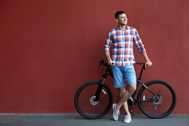 Handsome man with modern bicycle near red wall outdoors - Valokuva, kuva