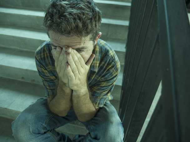 dramatyczny portret młody przygnębiony i smutny człowiek siedzący na zewnątrz problem depresja cierpienie rozpaczliwy kryzys stres ulica - Zdjęcie, obraz