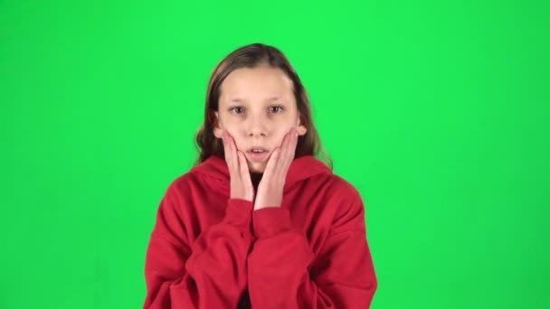Little female is scared and hiding her face in studio on green background. Slow motion - Кадри, відео