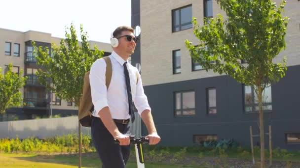 businessman with headphones riding scooter in city - Materiał filmowy, wideo