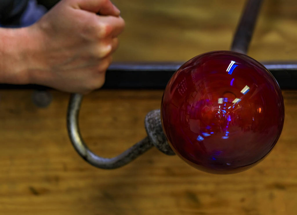 Glass blower shaping a bubble of melted glass on a rod by hand at a glass maker's workshop, shallow depth of field - Photo, Image
