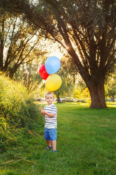 Park açık renkli balonlar ile sevimli sevimli küçük Kafkas çocuk yürümeye başlayan çocuk. Çocuk oynamaktan hoşlanıyor. Mutlu doğum günü tatili kutlaması. Samimi otantik yaşam tarzı çocukluk anı. - Fotoğraf, Görsel