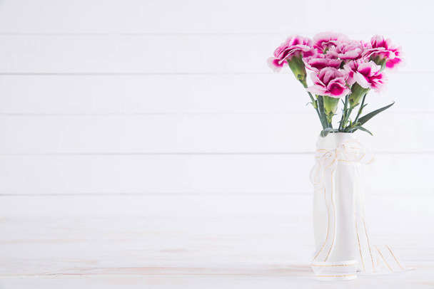 バレンタインの日、愛のコンセプトです。木製の白い背景の上に花瓶でピンクのカーネーションの花. - 写真・画像