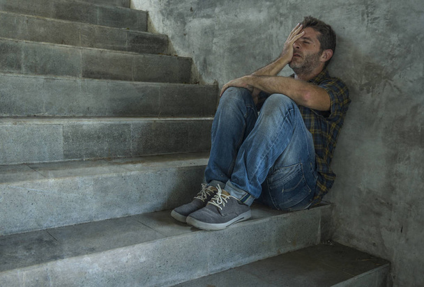 dramatic portrait of young depressed and desperate man sitting outdoors on dark grunge street corner staircase feeling sick suffering depression problem and anxiety crisis - Foto, Imagem
