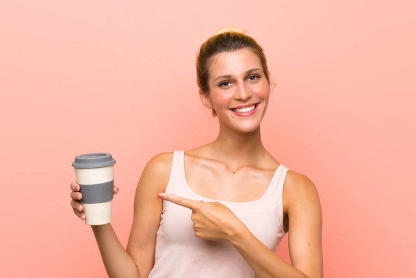 Young blonde woman holding a take away coffee and pointing it - Photo, Image