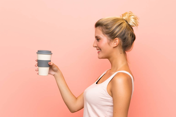 Joven mujer rubia sosteniendo un café para llevar con expresión feliz
 - Foto, Imagen