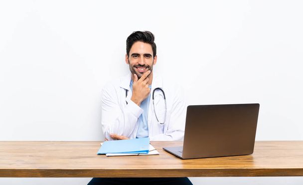 Junger Arzt lacht mit Laptop über isolierte Wand - Foto, Bild