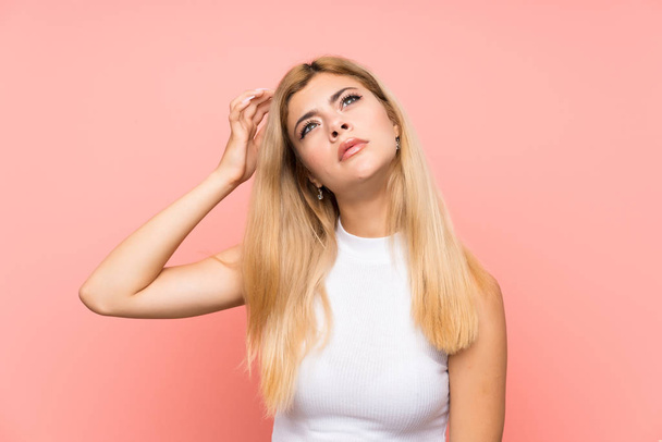 Teenager girl over isolated pink background having doubts and with confuse face expression - Photo, image