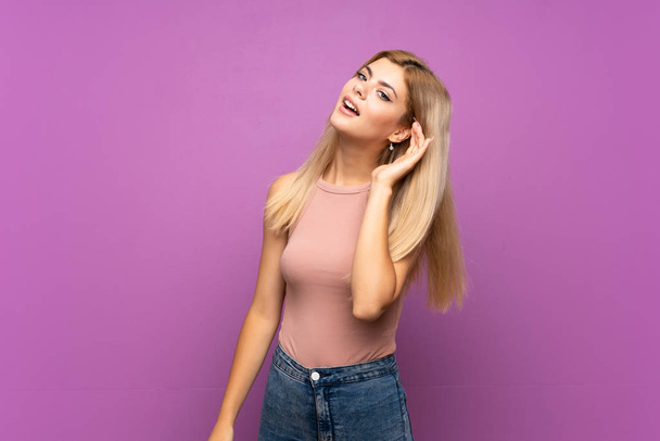 Teenager girl over isolated purple background listening to something by putting hand on the ear - Foto, Imagem