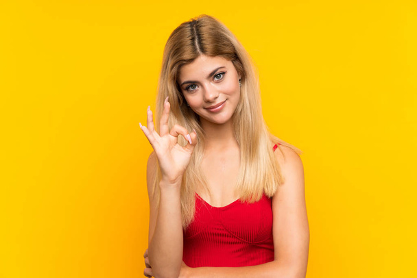 Teini tyttö yli eristetty keltainen tausta osoittaa ok merkki sormilla
 - Valokuva, kuva