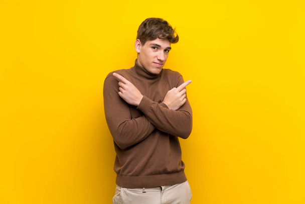 Handsome young man over isolated yellow background pointing to the laterals having doubts - Photo, image