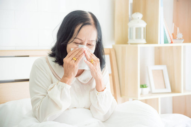 Unwell starszy kobieta dmuchanie nosa w łóżku, Starsza kobieta obejmujące nos z papieru tkankowego - Zdjęcie, obraz