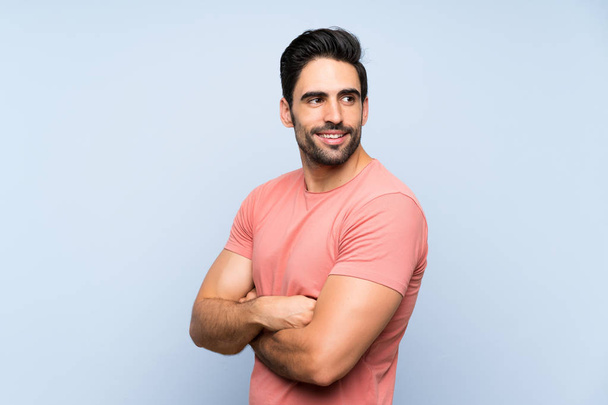 Handsome young man in pink shirt over isolated blue background with arms crossed and happy - Photo, Image