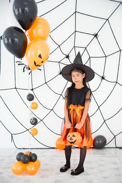Pretty girl in witch costume standing and holding pumpkin bucket - Фото, изображение