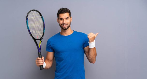 Handsome young tennis player man pointing to the side to present a product - Photo, Image