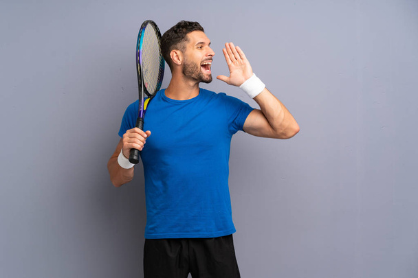 Handsome young tennis player man shouting with mouth wide open - Photo, Image